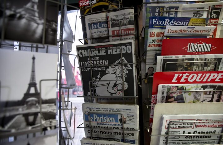 epa05089592 A copy of French satirical newspaper Charlie Hebdo's one-year anniversary edition of last year's January attacks in displayed in a kiosk in Paris, France, 06 January 2016. France this week commemorates the victims of last year's Islamist militant attacks on satirical weekly Charlie Hebdo and a Jewish supermarket with eulogies, memorial plaques and another cartoon lampooning religion. The cover of the special issue No. 1224 of the French satirical weekly Charlie Hebdo with a cartoon of a bearded god carrying a kalashnikov reading '1 an apres. L'assassin court toujours' (lit: One year later.The murderer is still on the run).  EPA/IAN LANGSDON