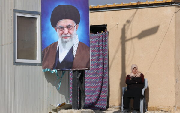 epa12636509 A refugee woman sits next to a portrait of Iranian Supreme Leader Ayatollah Ali Khamenei outside her makeshift shelter at the Imam Ali Complex in Hermel, Bekaa Valley, near the border with Syria, northeastern Lebanon, 08 January 2026. The housing project, inaugurated on 11 December 2025, is a donation from Iran and was carried out under the supervision of Iranian engineers. It consists of 228 residential units housing at least 900 refugees, most of whom are Lebanese and Syrians from villages along the border who fled following the fall of the Syrian regime of ousted president Bashar al-Assad.  EPA/WAEL HAMZEH