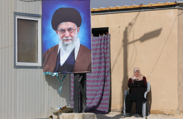 epa12636509 A refugee woman sits next to a portrait of Iranian Supreme Leader Ayatollah Ali Khamenei outside her makeshift shelter at the Imam Ali Complex in Hermel, Bekaa Valley, near the border with Syria, northeastern Lebanon, 08 January 2026. The housing project, inaugurated on 11 December 2025, is a donation from Iran and was carried out under the supervision of Iranian engineers. It consists of 228 residential units housing at least 900 refugees, most of whom are Lebanese and Syrians from villages along the border who fled following the fall of the Syrian regime of ousted president Bashar al-Assad.  EPA/WAEL HAMZEH